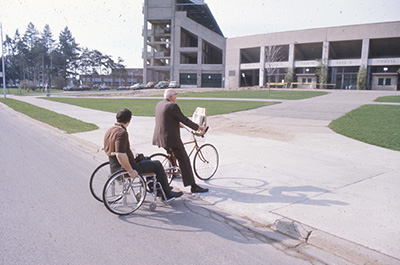 A man on a bike and another man in a wheelchair using the curb cut at MSU Spartan Stadium