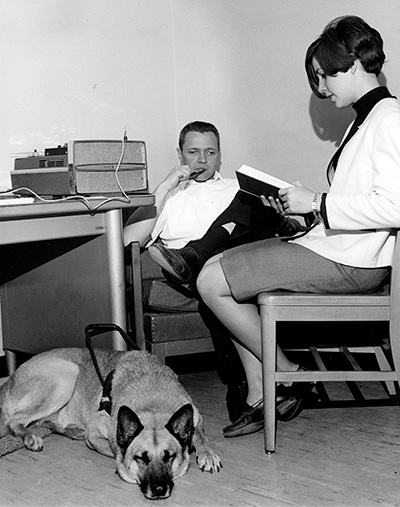 A woman reading to a man with a dog resting next to her