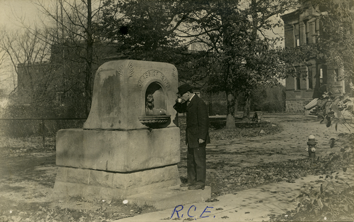 Historical image of man drinking from cup in front of a fountain at MSU