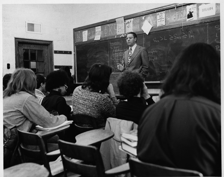 MSU President Clifton Wharton stands at the front of a classroom speaking to a large group of students.